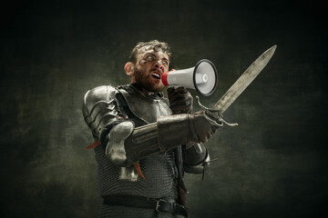 One brutal bearded man, medeival warrior or knight with loudspeaker over dark background.
