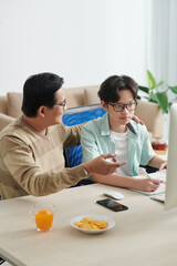 Smiling father hugging his son and explaining his difficult math topic on computer screen