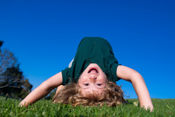 Happy child playing upside down on green grass. Funny kid outdoor in spring garden. Children day....