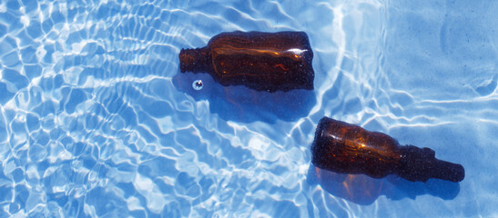 Brown glass oil bottle under fresh water on a blue background. Aromatherapy and perfumes concept
