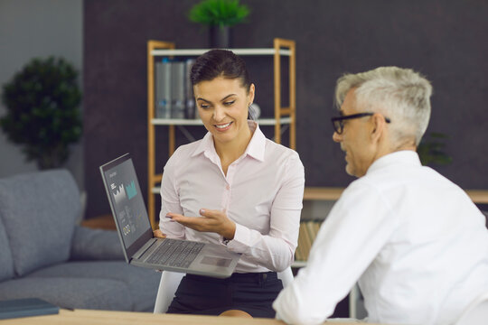 Smiling Bank Agent Or Financial Company Expert Meeting Client In Office, Showing Percentage Figures On Laptop Screen, Explaining Business Deal Details, Offering Loan Or Fixed Deposit With Good Returns