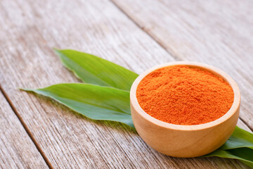 Turmeric powder in wooden bowl with green leaves isolated on wooden table background. 