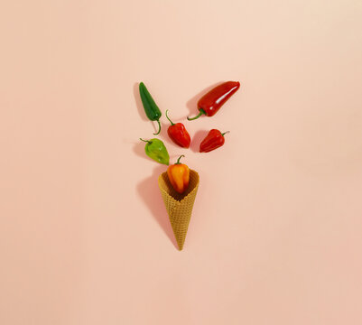 Jalapeno and habanero hot chili peppers in ice cream cone. Minimal flat lay composition on pastel pink background