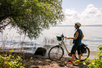 Frau mit Elektro Fahrrad steht am Ufer des Bodensee, genießt die Sommerfrische dieser schönen Reiseregion.
