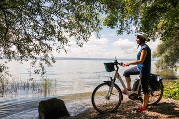Frau mit Elektro Fahrrad steht am Ufer des Bodensee, genießt die Sommerfrische dieser schönen...