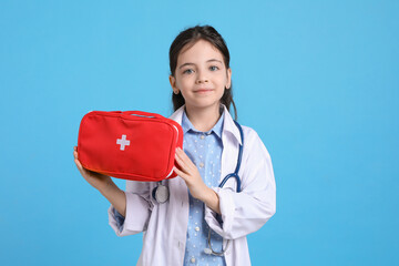Little girl with first aid bag and stethoscope dressed as doctor on light blue background. Pediatrician practice