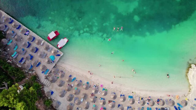 Aerial top down view of magnificent beach with clear blue water and white sand. People on vacation sunbathe and swim, summer vacation at the sea. Aerial drone shot of Ksamil, Albania