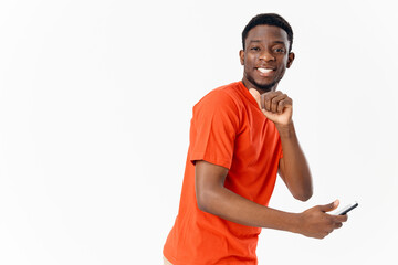 happy guy with mobile phone african appearance orange t-shirt light background Copy Space