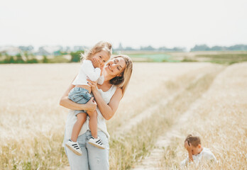 Mother holding a little smiling girl at the wheat field.