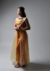 Full length portrait of pretty young asian woman wearing golden Arabian robes like a genie, holding...