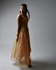 Full length portrait of pretty young asian woman wearing golden Arabian robes like a genie, holding...