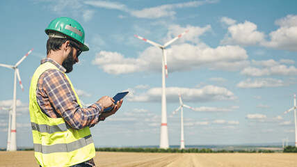 Electric engineer inspecting windmill turbine with tablet