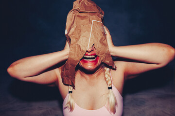 Blond woman with braids and smeared red lipstick, screaming in distress under old paper bag...