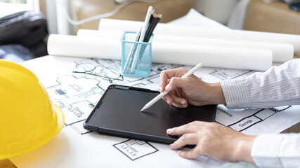 Young man using tablet plotting a system of building structures in blueprints, Architects or engineers are designing buildings using tablet to calculate the physical structure to be correct.