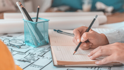 Architectural building design and construction plans with blueprints, young man is taking notes and...