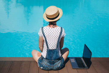 Woman working on her laptop computer sitting at poolside. ummer day near the beach resort, freelance concept