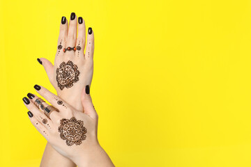Woman with henna tattoos on hands against yellow background, closeup and space for text....