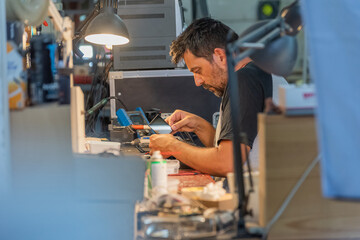 Side view of a middle-aged Caucasian man disassembling a camera screen in the service shop.