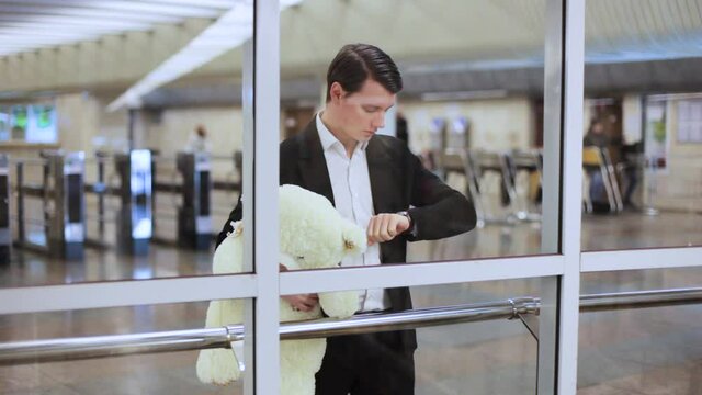 The young guy looks at his watch. He waits and worries. In his hands is a toy bear.