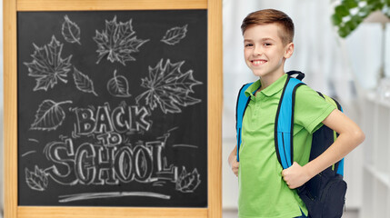 education, learning and people concept - happy smiling student boy with bag over chalkboard with...