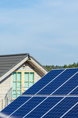 Solar panels on the field in the countryside with house on background. Solar power plant. Blue solar panels. Alternative source of electricity. Solar farm. Vertical