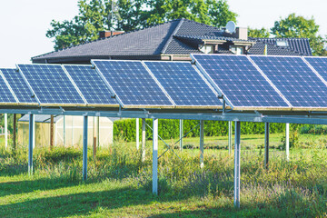Solar panels on the field in the countryside with house on background. Solar power plant. Blue solar panels. Alternative source of electricity. Solar farm