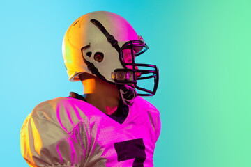 Cropped image of one American football player in sports equipment helmet and gloves isolated on blue studio background in neon light. Concept of sport, competition