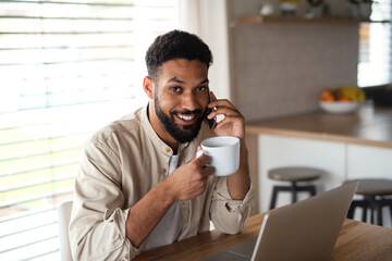 Young man student with laptop and smartphone working indoors at home, home office concept.