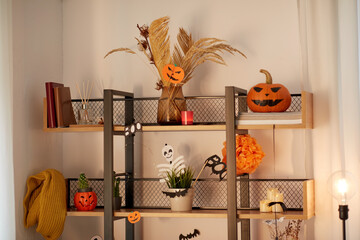 holidays, celebration and party concept - jack-o-lantern or carved pumpkin and other halloween decorations on shelf at home