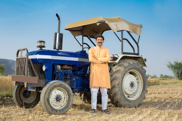 Happy Indian farmer with tractor on agricultural field
