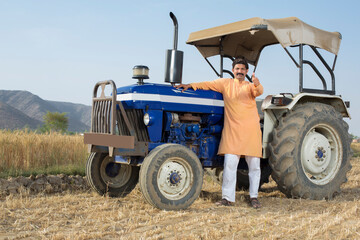 Happy Indian farmer with tractor on agricultural field