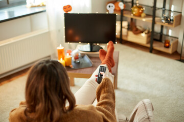 halloween, holidays and leisure concept - young womanwith remote control watching tv and resting...