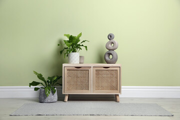 Wooden chest of drawers with decor and houseplants near light green wall indoors