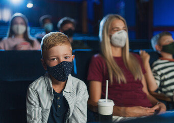 Small boy with mother looking at camera in the cinema, watching movies and coronavirus concept.