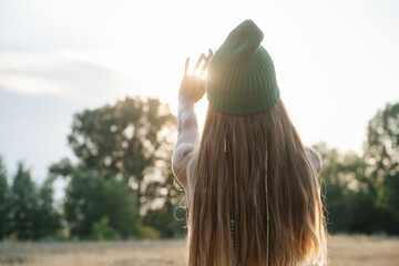 Long-haired woman in a green watch cap blocking sun with her hands.