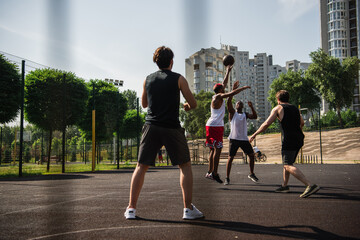 Young multiethnic sportsmen jumping while playing basketball on playground