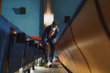 Young man cleaner sweeping floor in the cinema after the film, coronavirus concept.