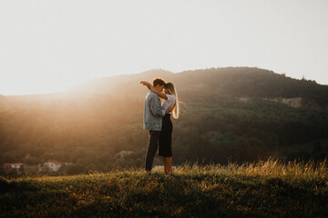 Young couple on a walk in nature at sunset in countryside, hugging.