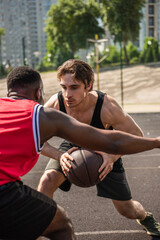 Young sportsman playing basketball with blurred african american friend during match