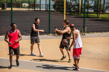 Positive interracial sportsmen with basketball balls talking outdoors