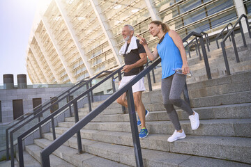 Middle aged couple, man and woman in sportswear walking down the stairs after exercising together outdoors
