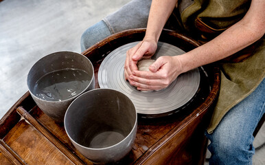 Woman working on the potter's wheel. Ceramist young woman making clay product on pottery lathe in studio. Close up of female hands working on potters wheel