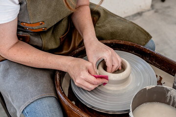 Woman working on the potter's wheel. Ceramist young woman making clay product on pottery lathe in studio. Close up of female hands working on potters wheel