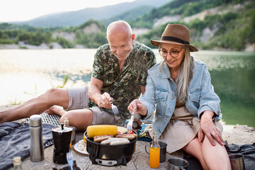 Happy senior couple resting on summer holiday trip, barbecue by lake.