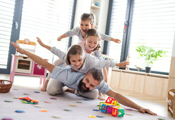 Father with three daughters indoors at home, playing on floor.