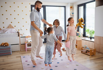 Father with three daughters indoors at home, playing on floor and jumping.