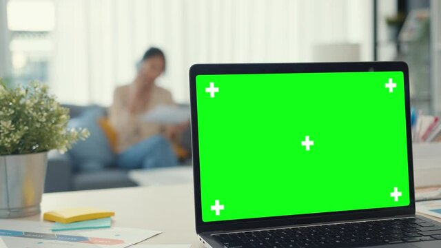 Computer laptop with blank green screen mock up display for advertising text on desk in living room at modern house. Chroma key technology, Marketing design concept.