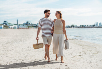 leisure, relationships and people concept - happy couple with picnic basket and blanket walking...