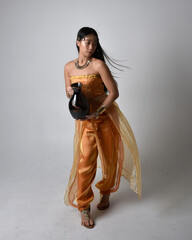 Full length portrait of pretty young asian woman wearing golden Arabian robes like a genie,...