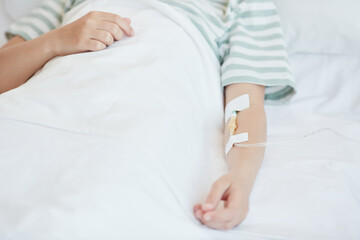 Close up of unrecognizable child in hospital bed with focus on IV drip in arm, copy space